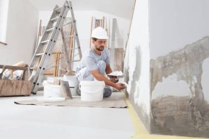 a guy painting white paint in bottom of wall of the room.