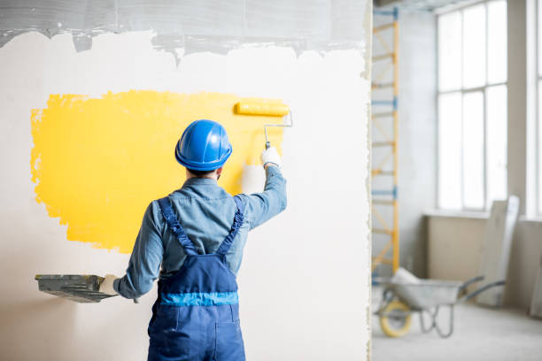 This person is painting the wall by painting brush with yellow colour.
